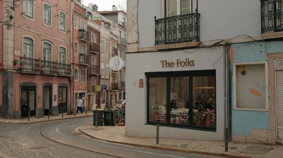 The street corner with The Folks in the foreground, a white building with large windows and logo in gold, and flowers inside the window.