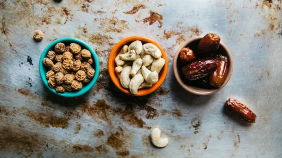 Three snack bowls, two with nuts, and one with dates.