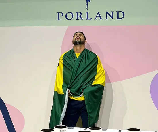 Dionatan awaits Championship results, wrapped in the Brazilian flag. His eyes are closed and his head is turned up.