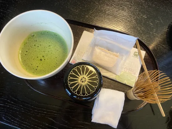 A bowl, whisk, curved wooden matcha scoop, and a small round object.