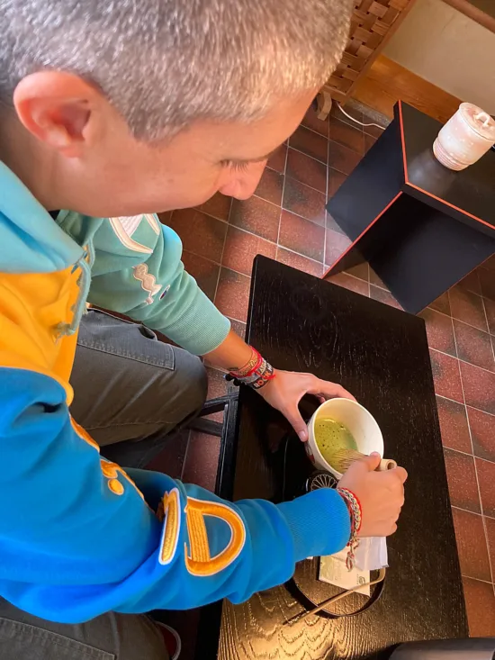 The author whisks match with water in a white bowl on a tray.